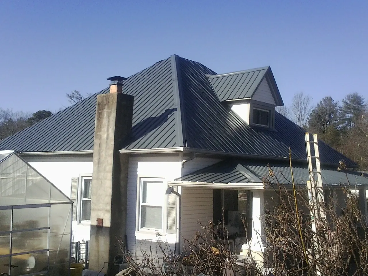 Dark blue standing seam metal roof on a white farmhouse with dormer — Slate & Tile Roof Repair by Roofing Brothers in Cedar Lake