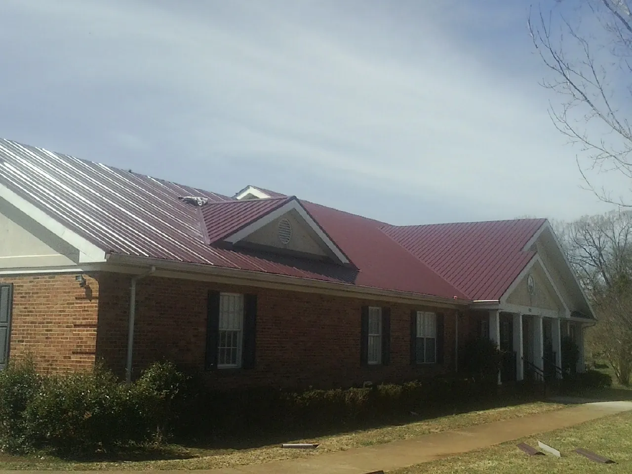 Red metal roof with gabled entries on a long brick building, from a Hail Damage Roof Repair job in Cedar Lake