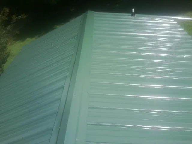New green metal panels meeting at the ridge of a roof — Flat Roof Repair work by our crew in Cedar Lake