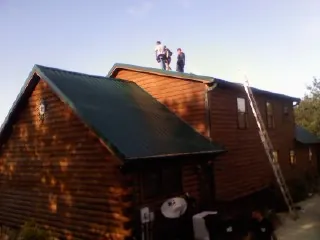 Crew on the ridge of a green metal roof on a two story log home in Cedar Lake