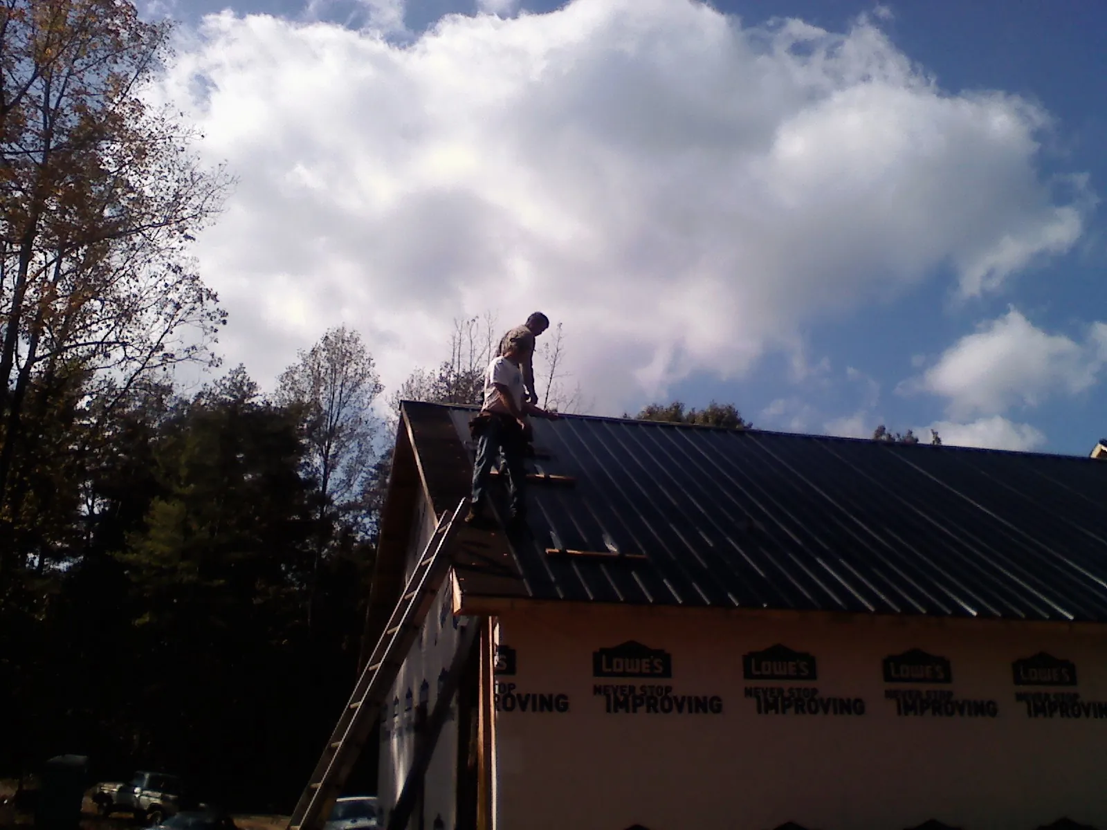 Roofer fastening dark metal panels high against a cloudy sky, from a Roof Inspection job in Cedar Lake