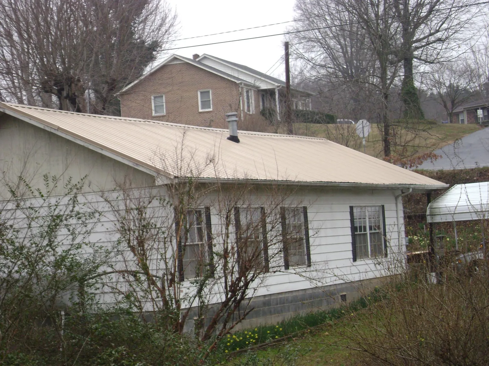 Tan metal roof on a white sided house set into a hillside — Commercial Roofing by Roofing Brothers in Cedar Lake